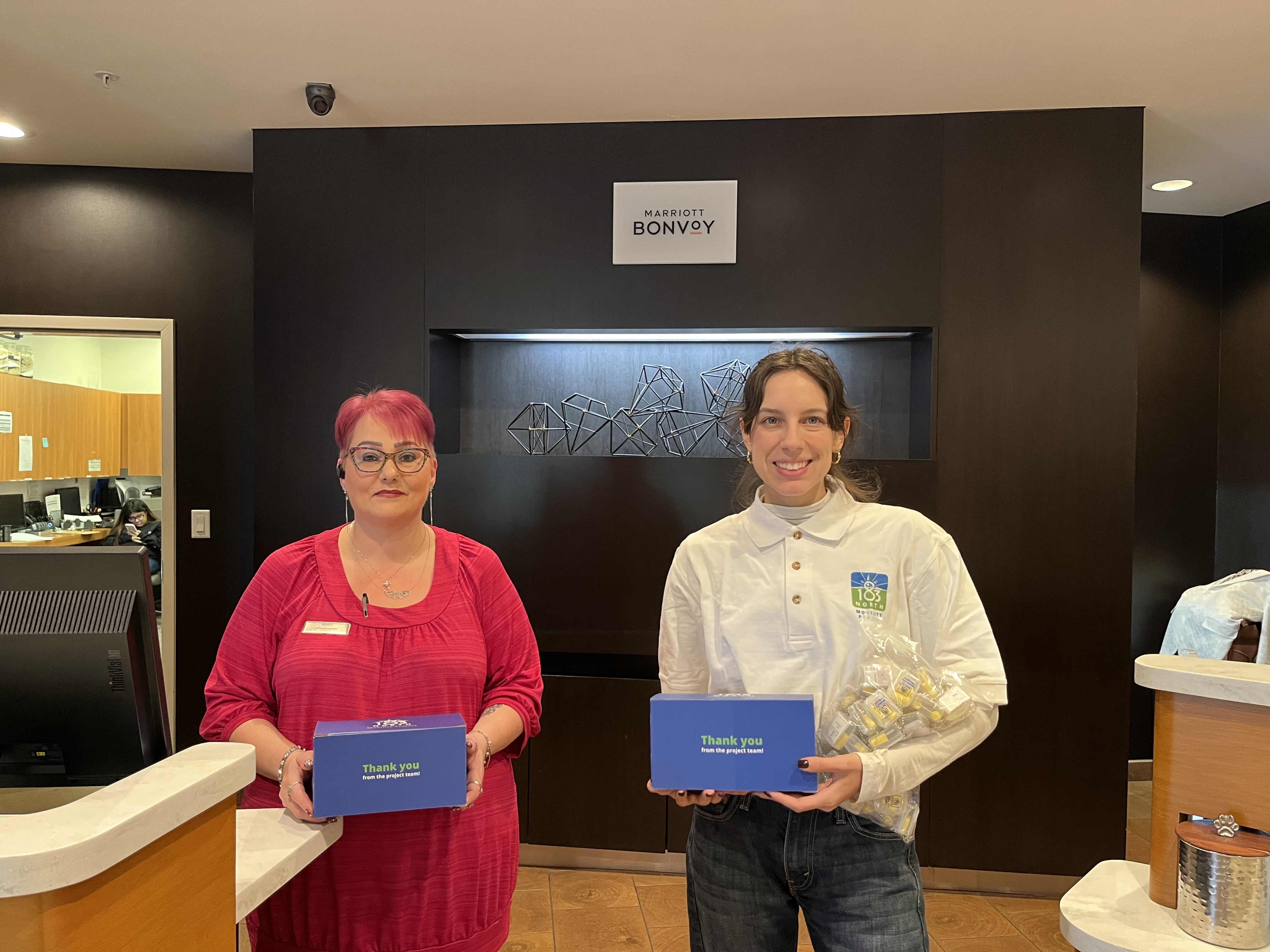 Two women pose for photo holding boxes of promo items