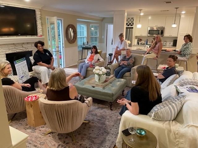A ground of women sit in a living area talking.