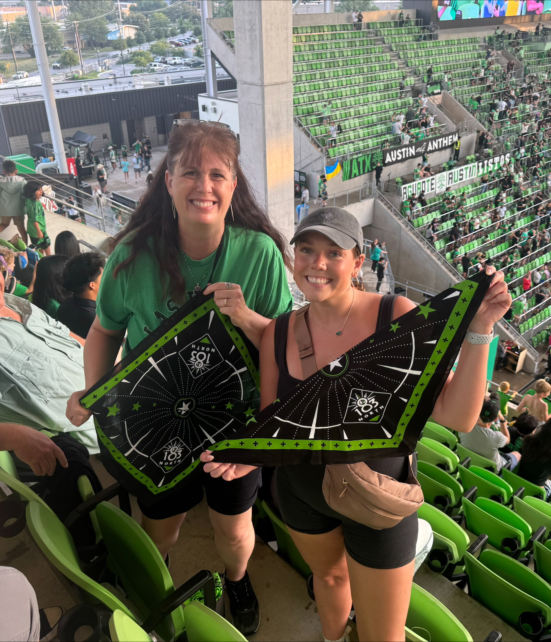 Two women hold up bandanas from their seats at a soccer stadium
